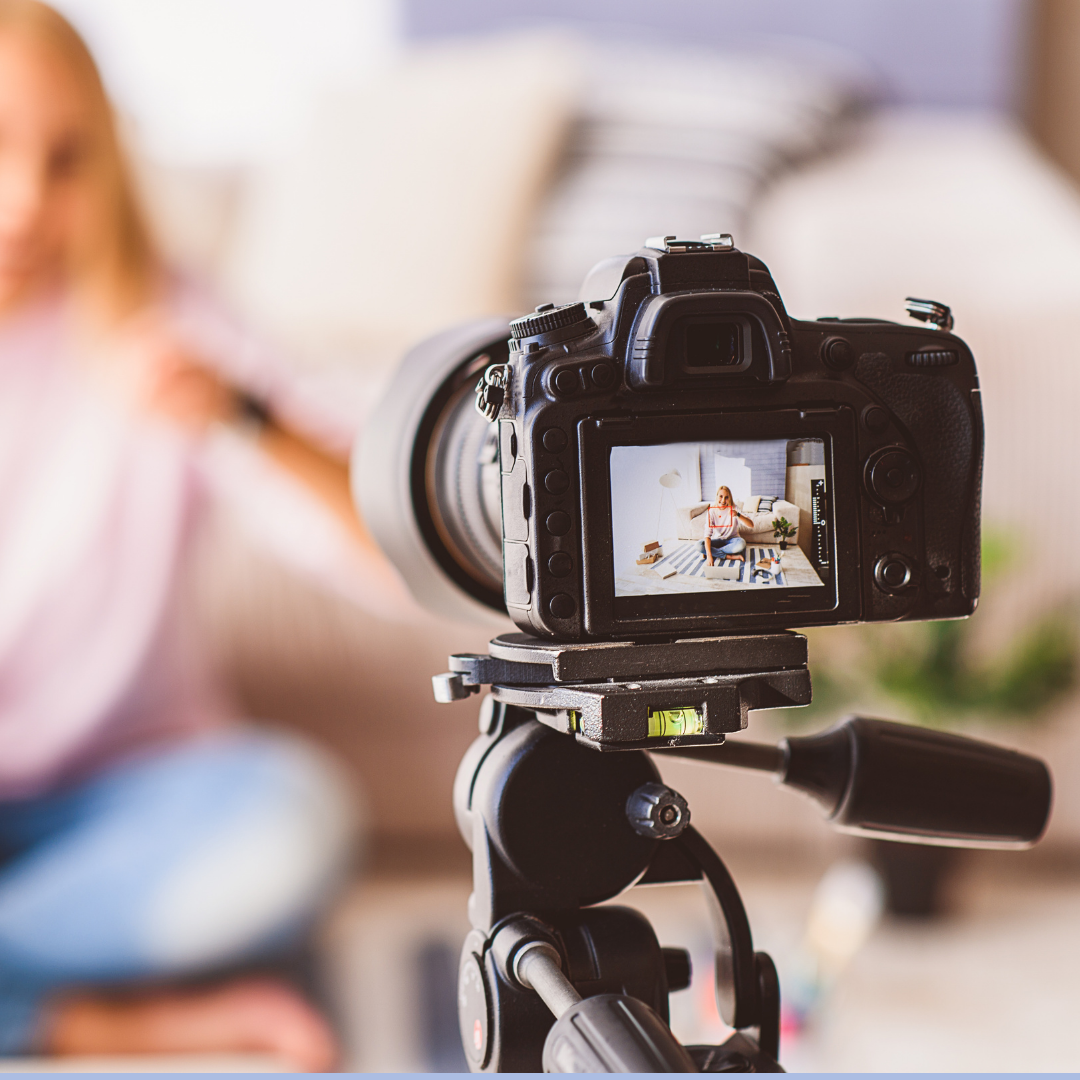 A video camera on a tripod recording a women that is sitting on her couch.