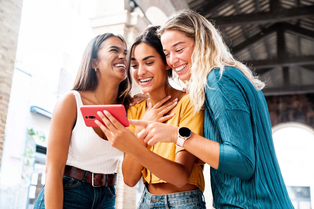 Three women smiling and looking at a phone together.