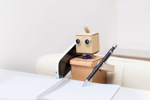 A robot using a phone and writing in a notebook with a pen.