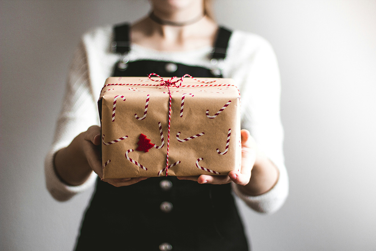 A person presenting a gift with holiday themed wrapping.